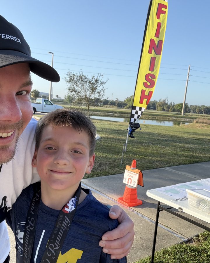 US Road Running race day photo with runners, walkers, finisher medals, and race staff